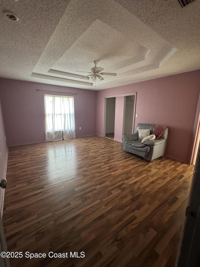 interior space with dark wood-type flooring, ceiling fan, a tray ceiling, a textured ceiling, and a closet