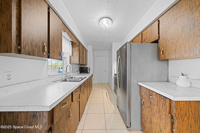 kitchen with light tile patterned floors, light countertops, a sink, a textured ceiling, and stainless steel fridge with ice dispenser