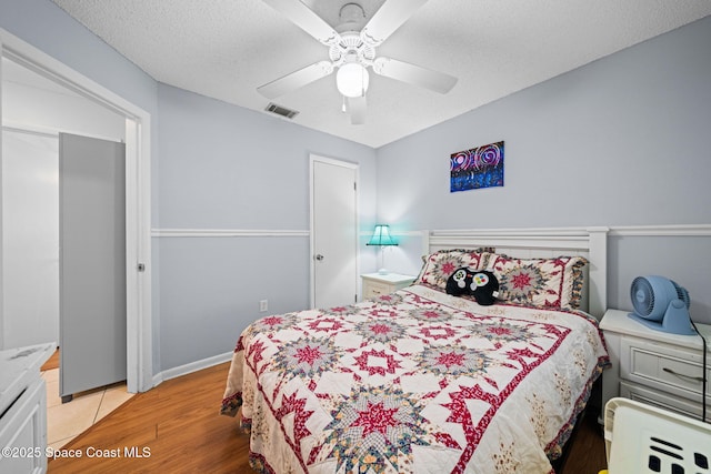 bedroom with light wood-style flooring, visible vents, ceiling fan, and a textured ceiling