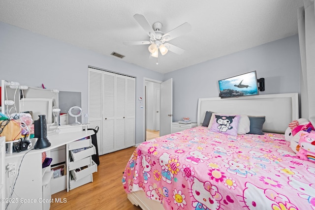 bedroom with a textured ceiling, a ceiling fan, visible vents, light wood-style floors, and a closet