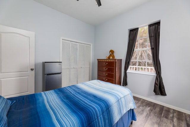 bedroom with multiple windows, stainless steel fridge, dark hardwood / wood-style flooring, and a closet