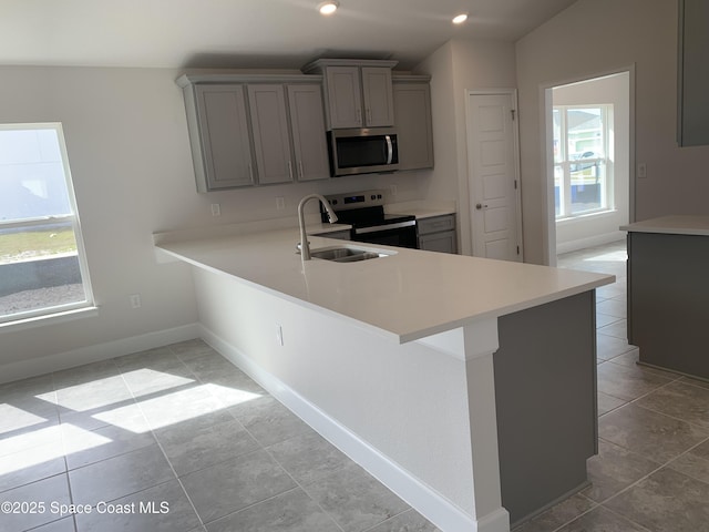 kitchen with gray cabinetry, vaulted ceiling, kitchen peninsula, and appliances with stainless steel finishes