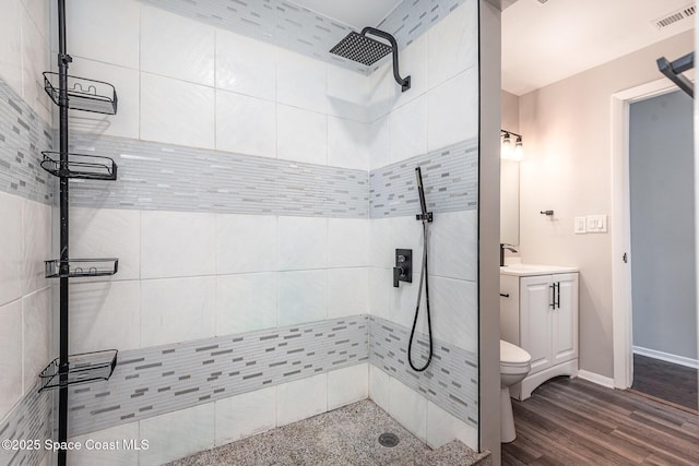 bathroom with hardwood / wood-style flooring, vanity, tiled shower, and toilet