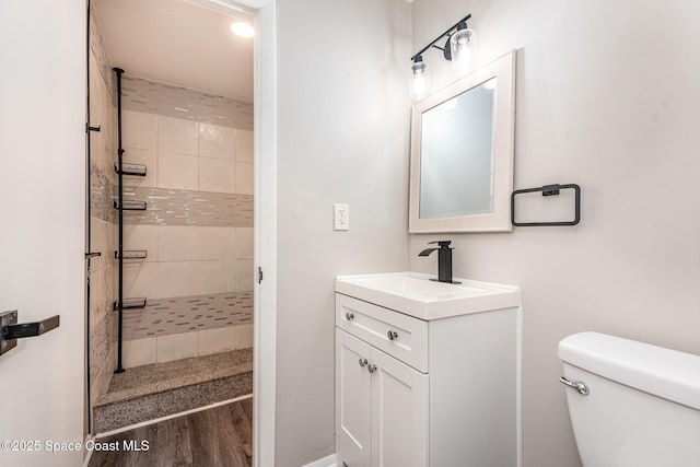 bathroom with vanity, hardwood / wood-style flooring, toilet, and tiled shower