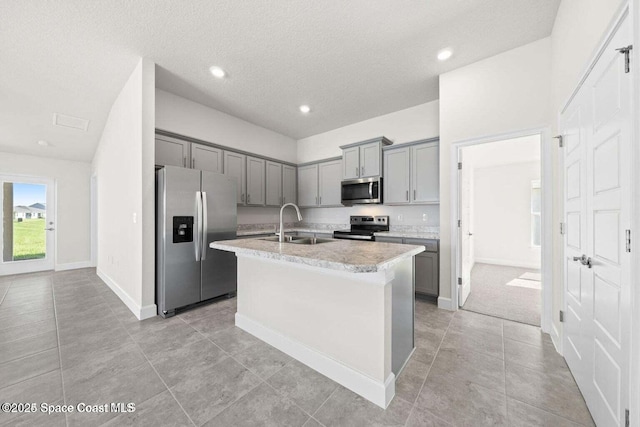 kitchen with stainless steel appliances, sink, a center island with sink, and gray cabinetry