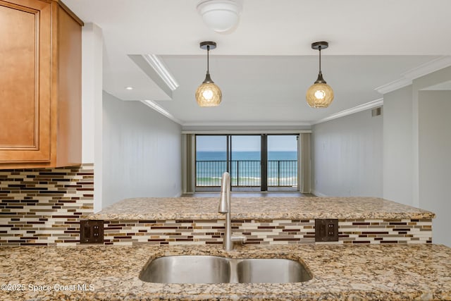 kitchen with sink, backsplash, a water view, crown molding, and light stone countertops