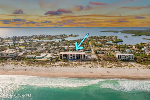 aerial view at dusk with a water view and a view of the beach