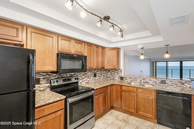 kitchen with sink, hanging light fixtures, light stone counters, black appliances, and a raised ceiling