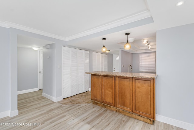 kitchen featuring hanging light fixtures, a raised ceiling, light stone countertops, and ornamental molding