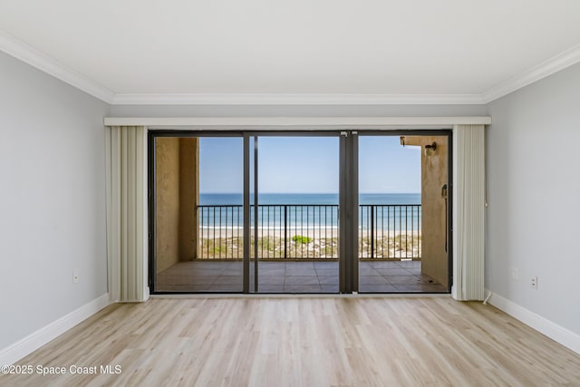 unfurnished room with a view of the beach, crown molding, light hardwood / wood-style flooring, and a water view