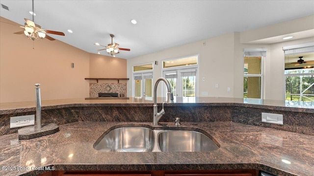 kitchen with a wealth of natural light, a fireplace, dark stone counters, and a sink