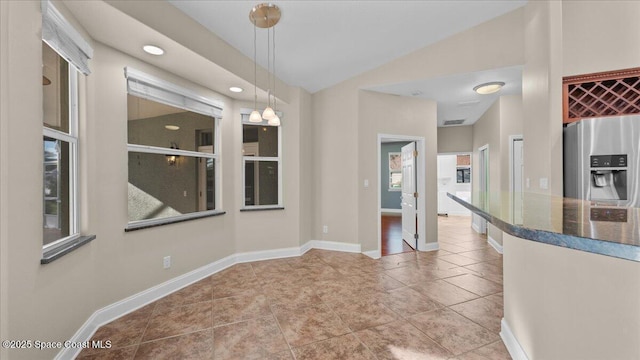 unfurnished dining area featuring lofted ceiling, tile patterned floors, and baseboards