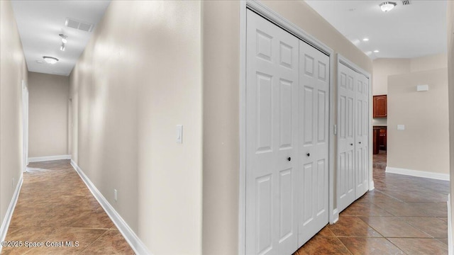 hall featuring visible vents, baseboards, and light tile patterned floors