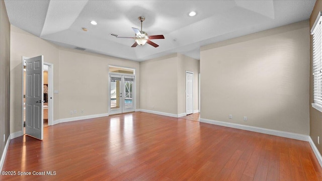 empty room with french doors, recessed lighting, a raised ceiling, hardwood / wood-style floors, and baseboards