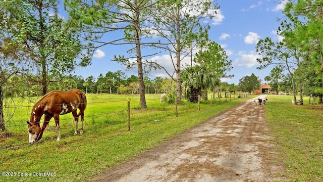 view of home's community featuring a rural view, fence, dirt driveway, and a lawn