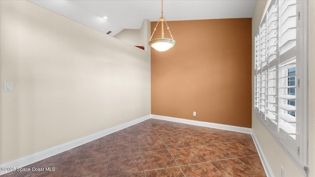 empty room featuring dark tile patterned flooring, lofted ceiling, and baseboards