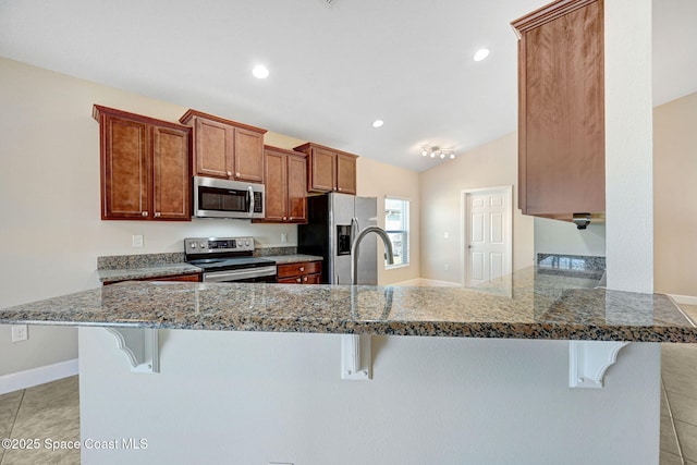 kitchen with appliances with stainless steel finishes, kitchen peninsula, vaulted ceiling, and a breakfast bar area