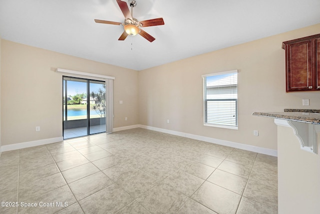 empty room featuring a wealth of natural light, light tile patterned flooring, ceiling fan, and a water view