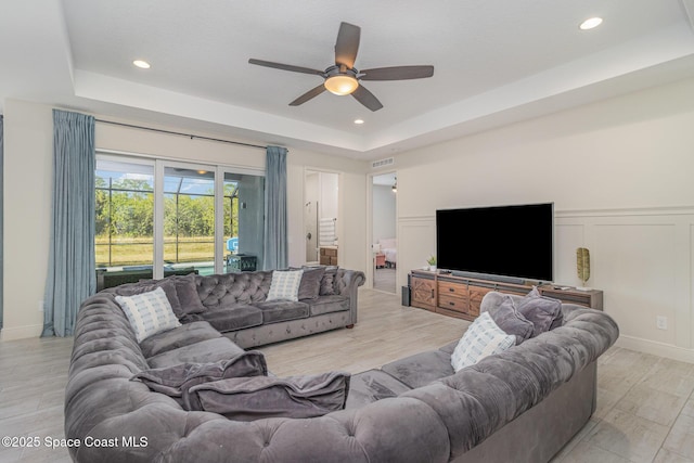 living room featuring ceiling fan, light wood-type flooring, and a tray ceiling