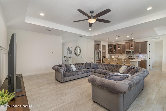 living room with a tray ceiling, a textured ceiling, and ceiling fan