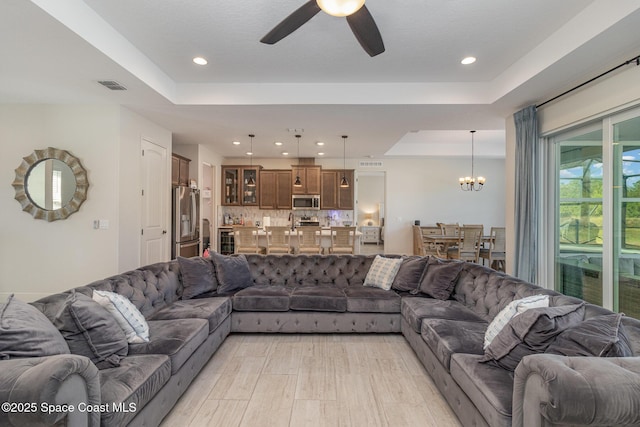 living room with ceiling fan with notable chandelier and a tray ceiling