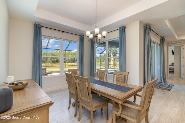 dining room with a raised ceiling, light wood-type flooring, and an inviting chandelier