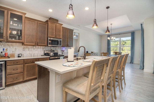 kitchen with a breakfast bar, a raised ceiling, tasteful backsplash, hanging light fixtures, and stainless steel appliances