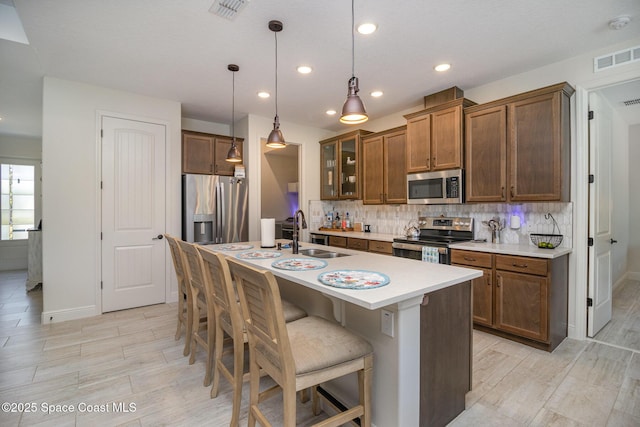 kitchen featuring sink, a breakfast bar area, decorative light fixtures, appliances with stainless steel finishes, and an island with sink