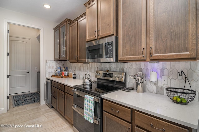 kitchen featuring decorative backsplash, stainless steel appliances, beverage cooler, and light wood-type flooring