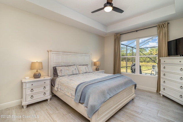 bedroom featuring ceiling fan, a raised ceiling, and light hardwood / wood-style floors