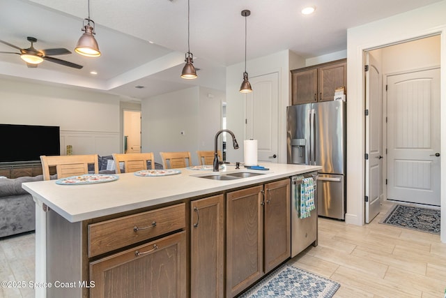 kitchen with pendant lighting, sink, stainless steel appliances, a tray ceiling, and an island with sink