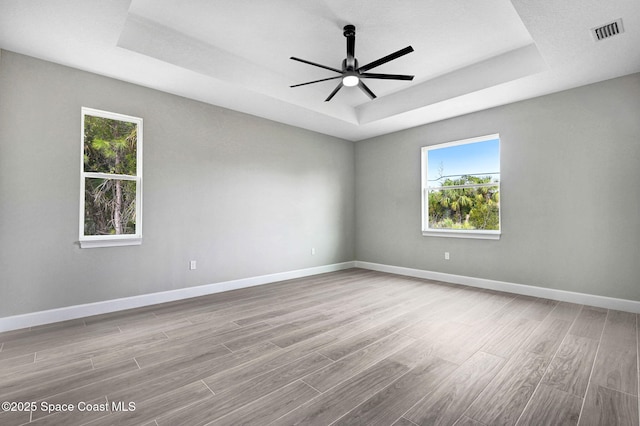 empty room with a raised ceiling, ceiling fan, and light wood-type flooring