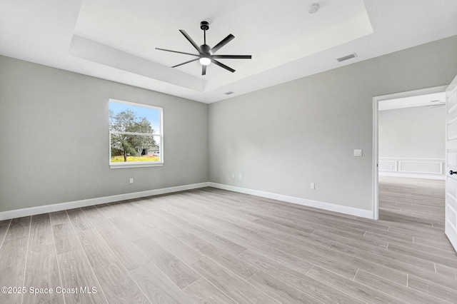 spare room featuring ceiling fan, a tray ceiling, and light hardwood / wood-style flooring