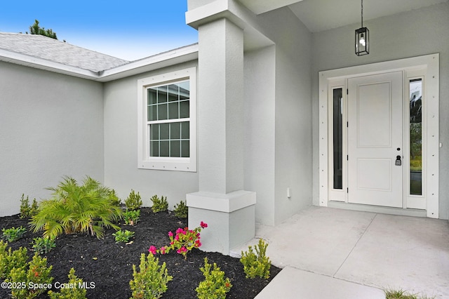 entrance to property featuring roof with shingles and stucco siding