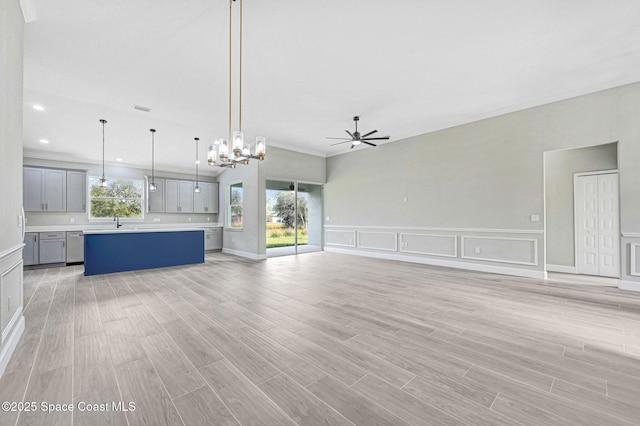 unfurnished living room featuring plenty of natural light, ceiling fan with notable chandelier, and light wood-type flooring