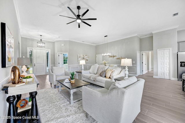 living room with baseboards, visible vents, crown molding, wood finish floors, and ceiling fan with notable chandelier