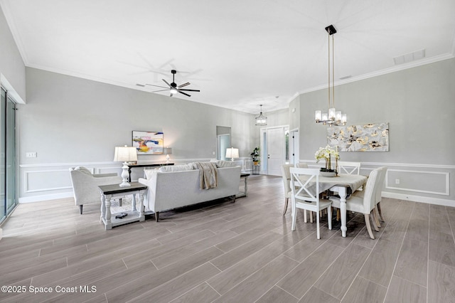 dining area with a decorative wall, ceiling fan with notable chandelier, wood finish floors, visible vents, and ornamental molding