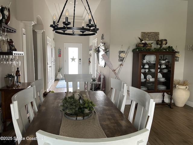 dining area featuring wood-type flooring, decorative columns, and a notable chandelier