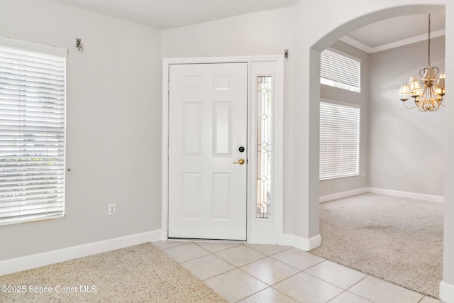 tiled foyer entrance featuring ornamental molding and a notable chandelier