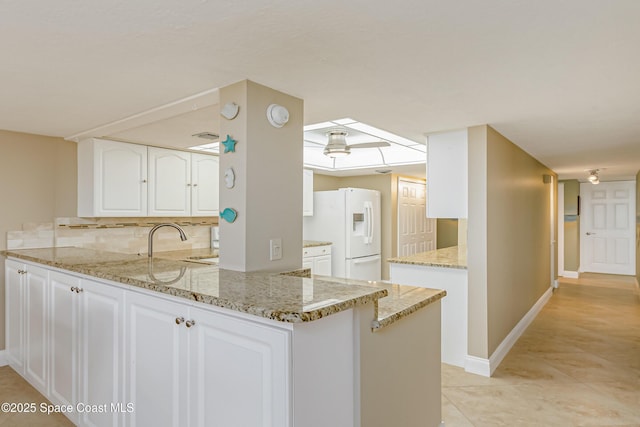 kitchen featuring white cabinets, kitchen peninsula, light stone countertops, and white fridge with ice dispenser