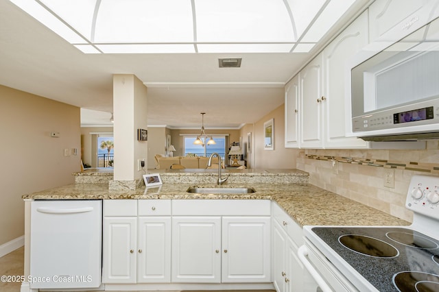 kitchen with decorative light fixtures, white cabinets, a sink, white appliances, and a peninsula