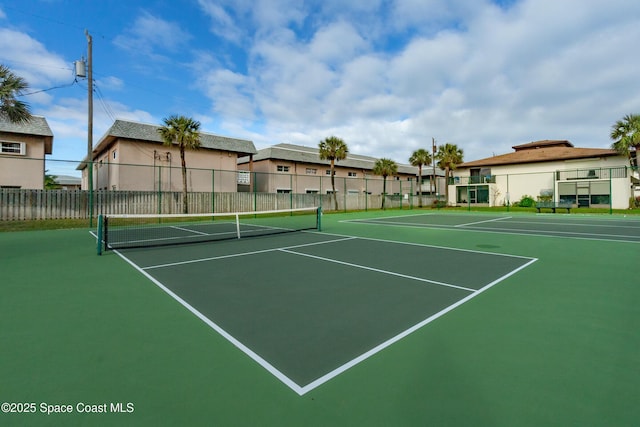 view of tennis court featuring community basketball court, fence, and a residential view