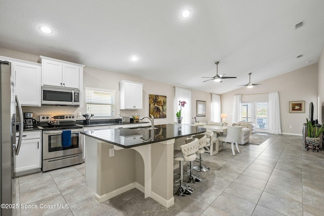 kitchen with an island with sink, sink, dark stone countertops, stainless steel appliances, and plenty of natural light