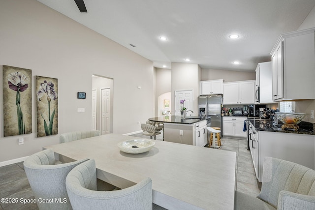 kitchen with stainless steel appliances, vaulted ceiling, a kitchen island with sink, and white cabinets