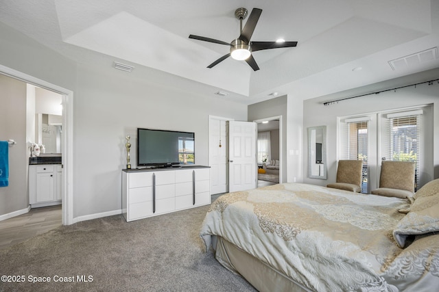 carpeted bedroom featuring a tray ceiling, ensuite bath, and ceiling fan