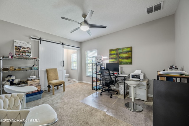 office area with a textured ceiling, light colored carpet, a barn door, and ceiling fan