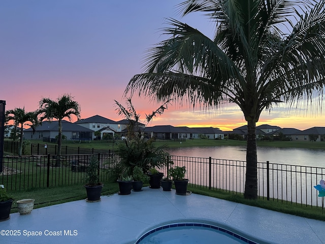 pool at dusk featuring a water view and a patio area