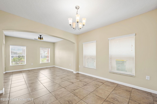 tiled empty room with a textured ceiling and a chandelier