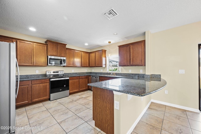 kitchen with sink, hanging light fixtures, appliances with stainless steel finishes, kitchen peninsula, and dark stone counters