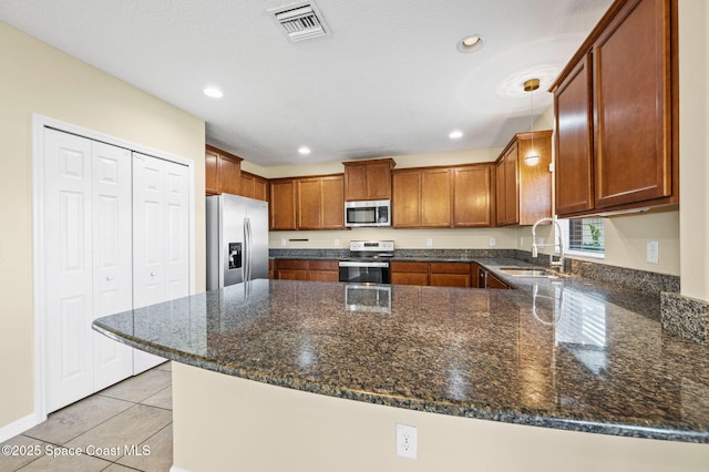 kitchen featuring sink, light tile patterned floors, stainless steel appliances, kitchen peninsula, and dark stone counters